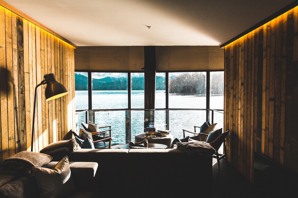 Interior of waterfront room with dark couches, chairs, fireplace, and large window